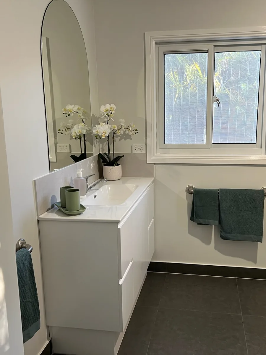 Bathroom with an arched mirror, white vanity and dark floor tiles