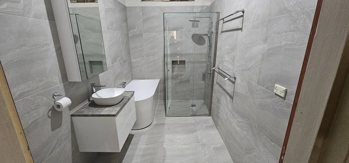 Ensuite with large grey stone-look tiles, frameless shower, freestanding bath and floating vanity