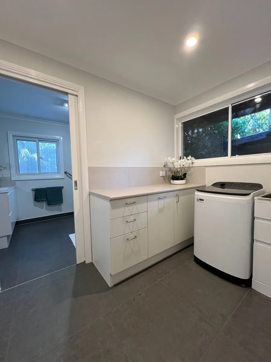 A white laundry with stone benchtop opening through to a bathroom